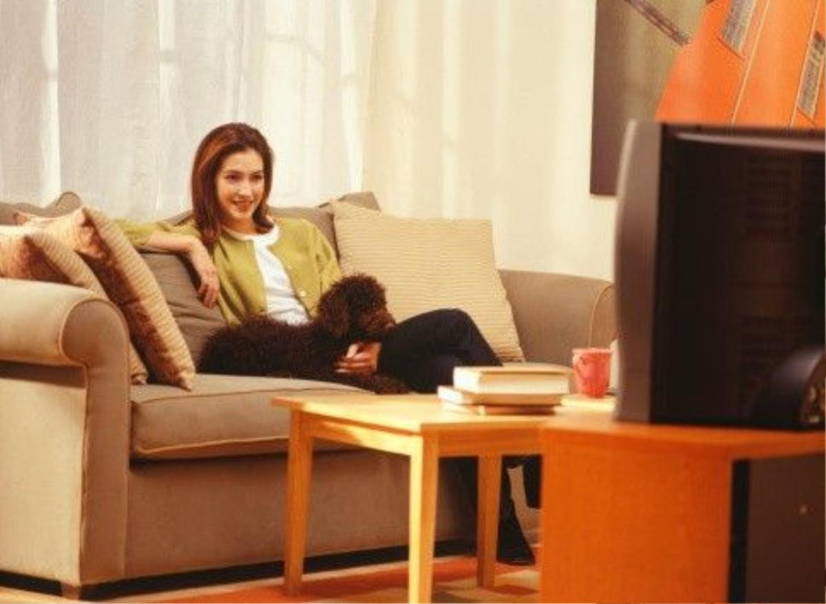 Young woman sitting on sofa with dog, watching television